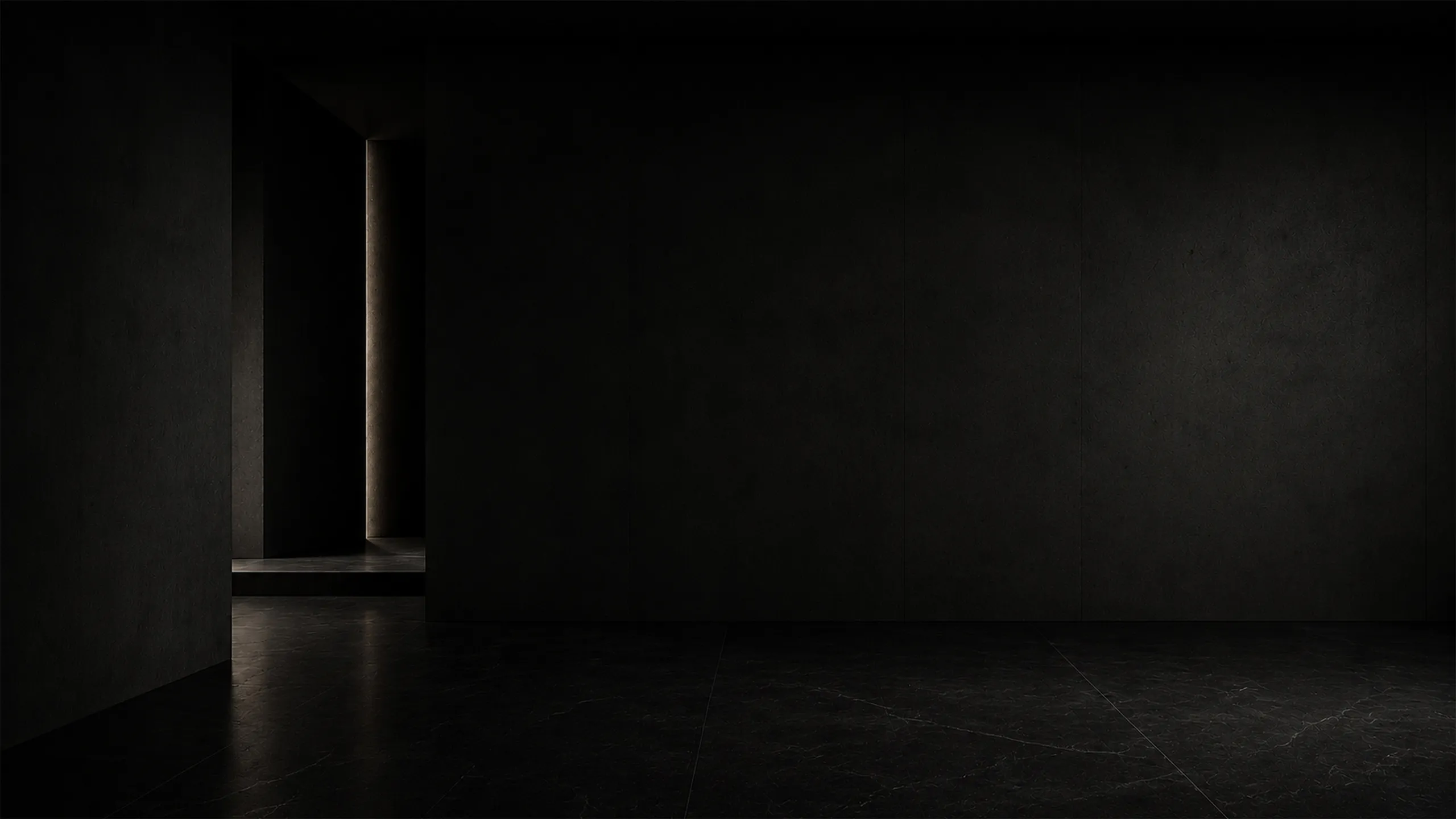 A nearly black architectural interior where a narrow vertical line of warm light reveals the depth, texture and proportions of the space.