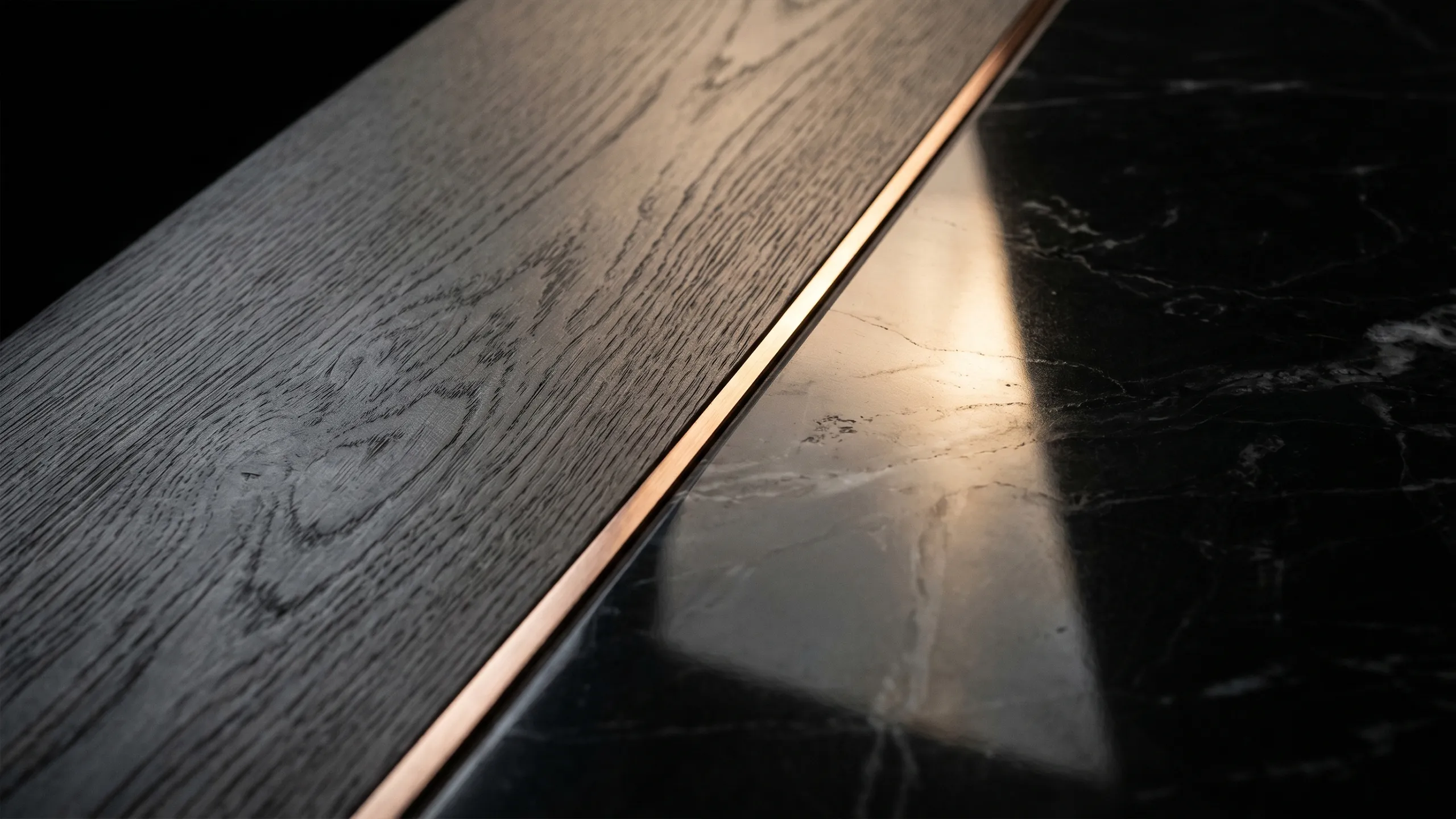 Close-up of a precise junction between dark timber, black stone and a narrow bronze inlay, illustrating material detailing and build quality.