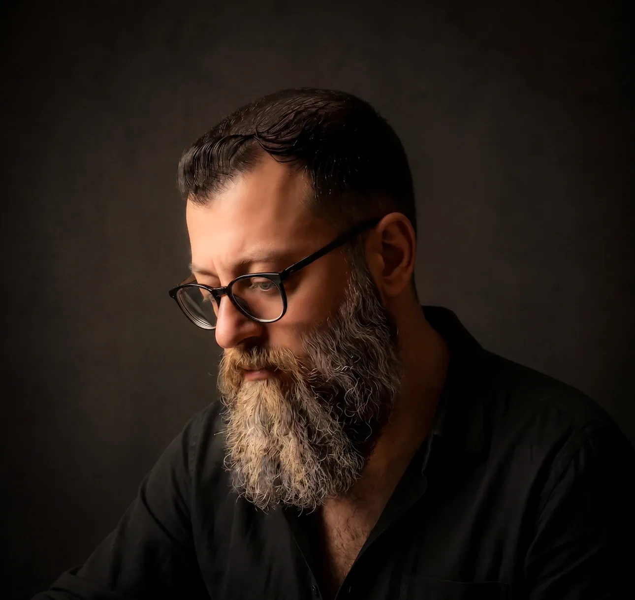 Portrait of Nariman Fatemi, a Dubai-based architect and artist, wearing glasses against a dark studio background.